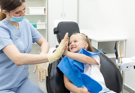 Child smiling while giving dental assistant high-five
