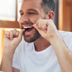 Man smiling while flossing his teeth in bathroom