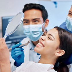Patient smiling at reflection with dental hygienist and dentist