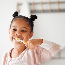 Child smiling while brushing their teeth in bathroom