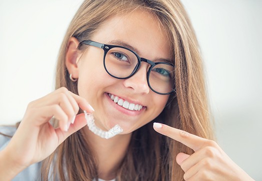 Smiling teenager pointing to Invisalign clear aligners in Arlington Heights 