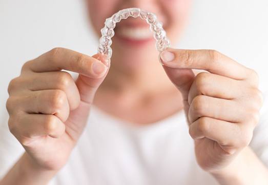 Smiling woman holding out Invisalign in Arlington Heights 