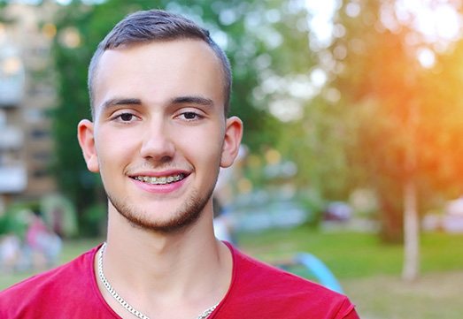 a person smiling and standing in a park with ceramic braces