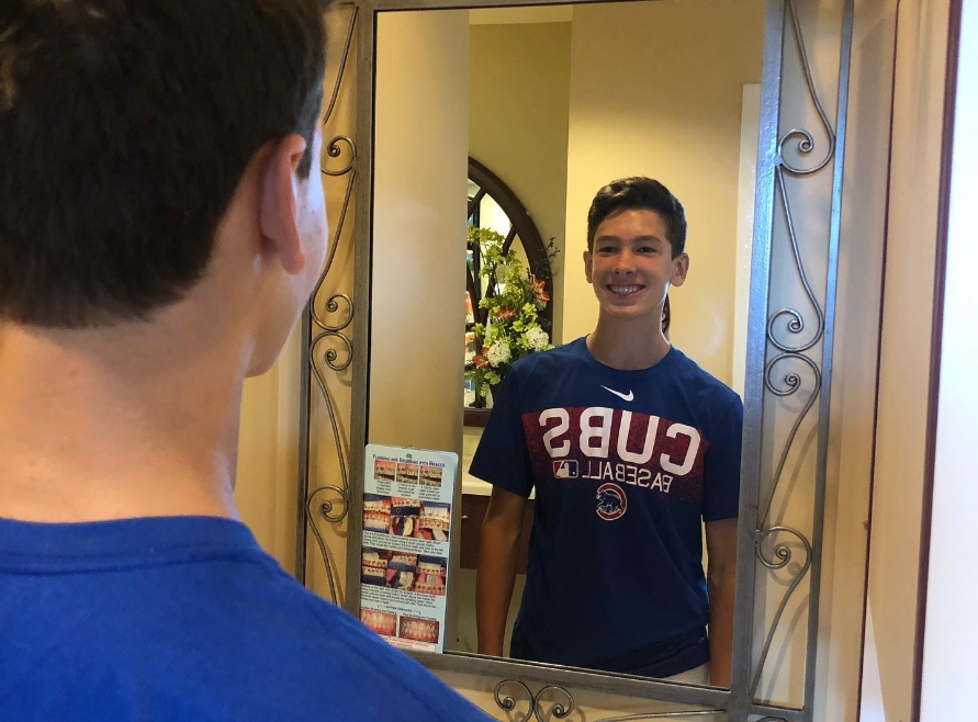 Young man looking at smile in mirror after visiting the pediatric dentist