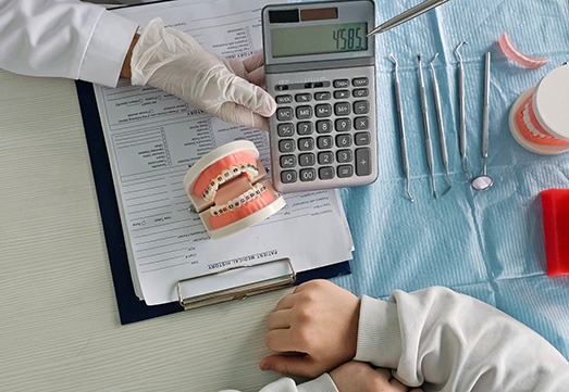 Bird’s eye view of gloved hand holding out calculator above forms with sample braces sitting on them