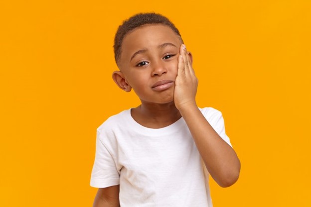 child suffering from oral sensitivity touching cheek