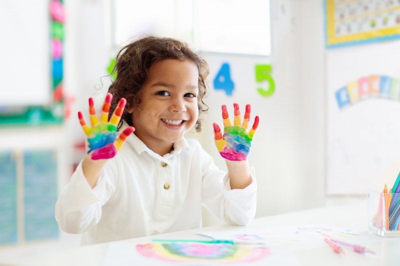 A child finger painting, smiling to show off her good dental health